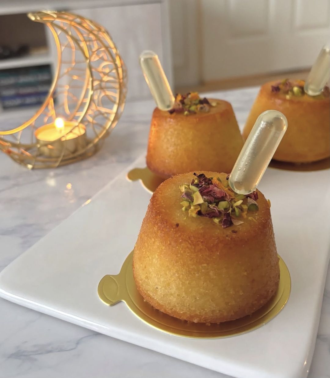 Golden basbousa cups topped with pistachio and rose petals, with pipettes of orange blossom syrup (photo 1 of 2)