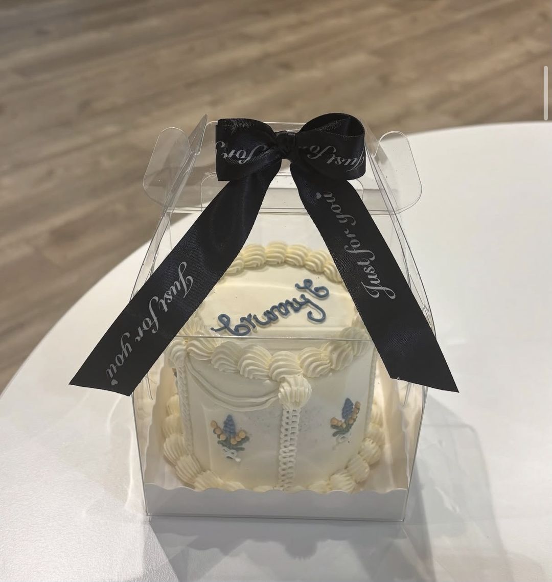 White bento cake with “Grumpy” piped in blue and blue flower details, boxed with a black ribbon (photo 1 of 2)