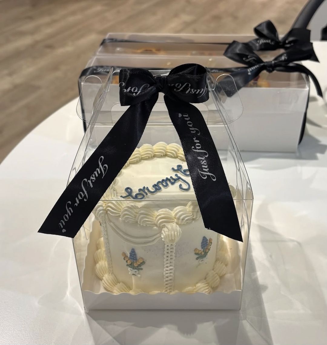 White bento cake with “Grumpy” piped in blue and blue flower details, boxed with a black ribbon (photo 2 of 2)