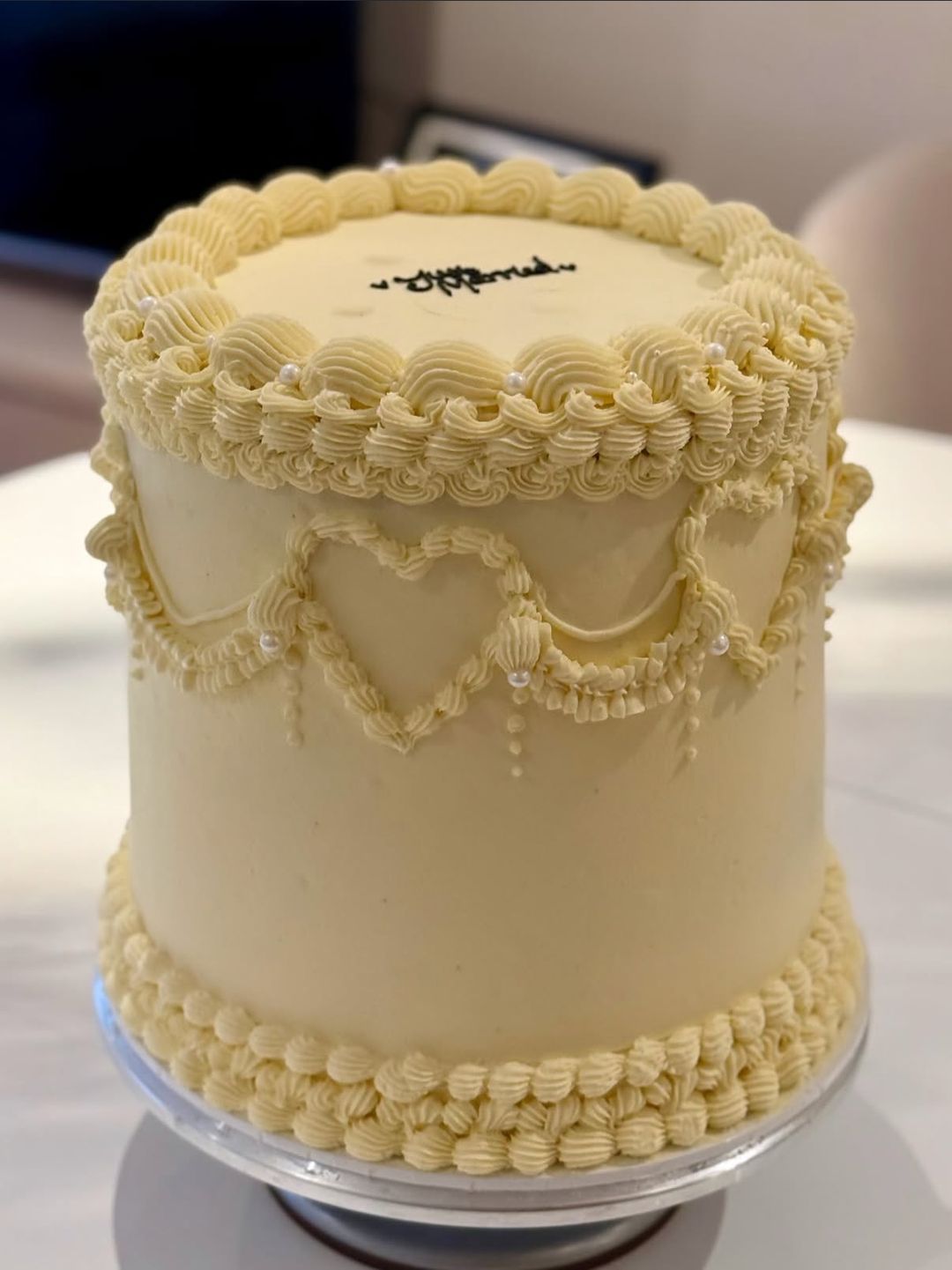 Tall butter-yellow vintage cake with piped heart garlands, pearl details and “Just married” on top
