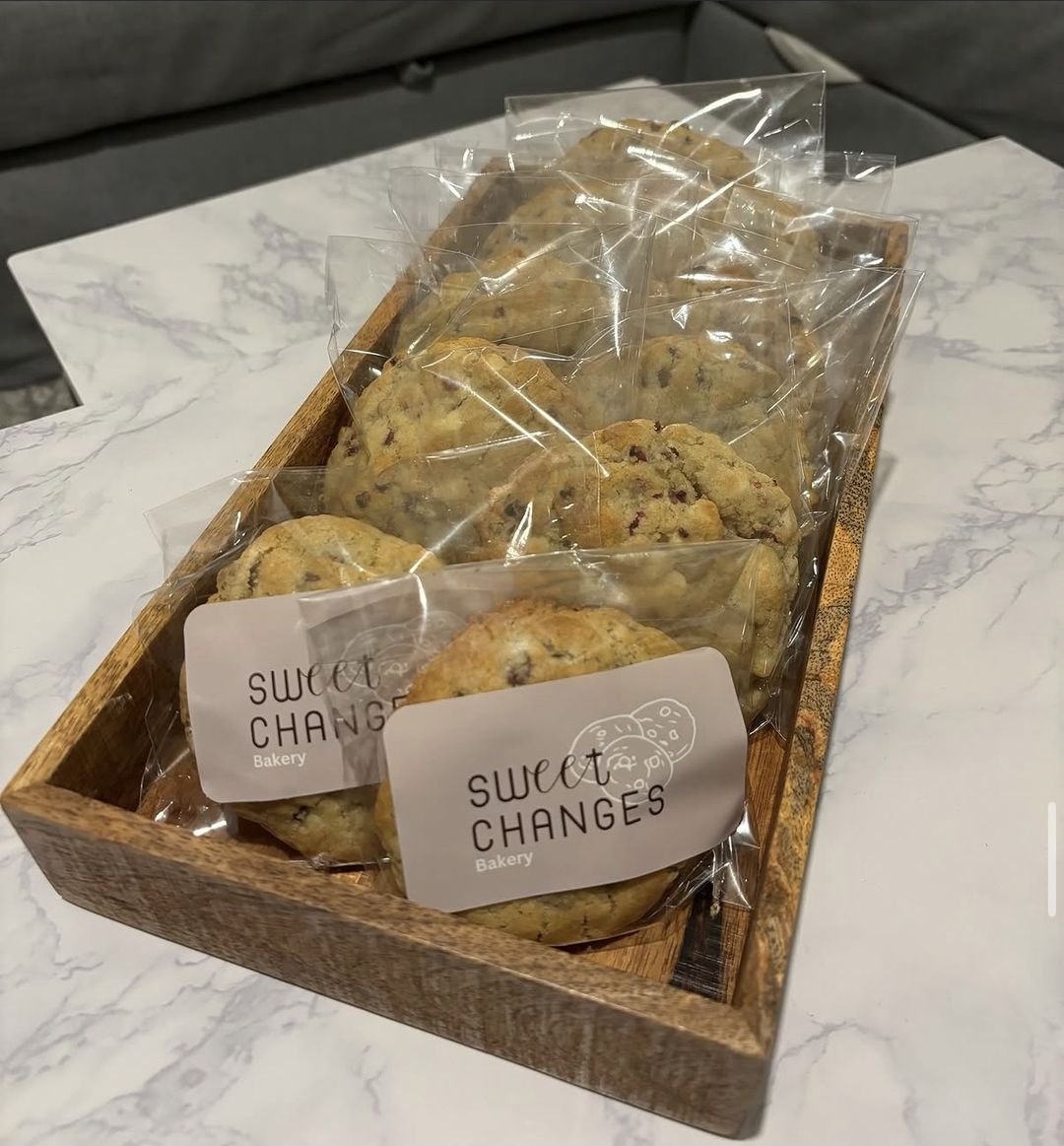NYC-style cookies wrapped in bags with Sweet Changes stickers, on a wooden tray